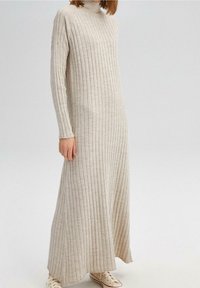 Robe maxi en tricot côtelé beige avec un col haut et des manches longues, présentant une coupe décontractée et un bord festonné subtil aux poignets.