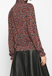 Langärmlige Bluse mit einem mehrfarbigen abstrakten Muster, weichem Stoff, steigendem Kragen und gerafften Manschetten, kombiniert mit einem schwarzen Lederröck.