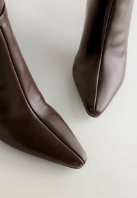 Brown leather ankle boots with a pointed toe design and smooth texture, featuring a sleek silhouette and minimal stitching details.