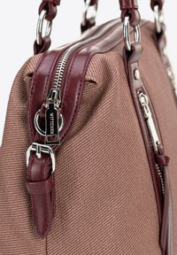 Brązowa torebka o fakturowanej powierzchni z burgundowymi skórzanymi akcentami i metalowymi elementami. Posiada zamek błyskawiczny oraz detale w postaci łańcuszka w uchwycie.