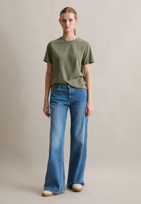 T-shirt à manches courtes vert olive associé à un jean large bleu clair. Le t-shirt a un col rond ; le jean présente un design classique à cinq poches.