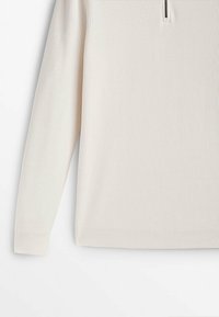 Pull côtelé couleur crème, avec une fermeture éclair au quart. La texture est douce, avec des manches longues et un ourlet ajusté.