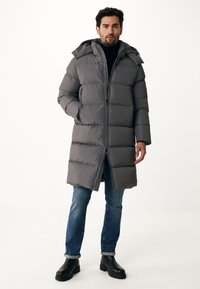 Abrigo de plumas gris con capucha, con secciones horizontales cosidas, cierre frontal y bolsillos laterales, llevado sobre un par de vaqueros azules y botas negras.