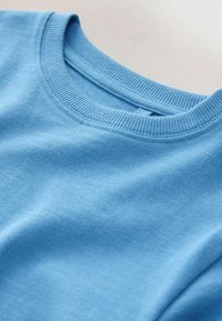 Világoskék pamut környakú pulóver bordázott mandzsettákkal és nyakkal, sima textúrával és látható minták vagy fém részletek nélkül.
