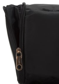 Sac en nylon noir avec une texture lisse, doté d'une tirette dorée et d'un compartiment zippé, affichant un design minimaliste.