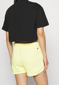 Black cropped t-shirt with short sleeves paired with bright yellow, elastic-waist shorts featuring a small black logo on the side.