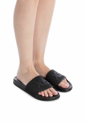 Chanclas de goma negras con una correa texturizada que presenta el logo, diseño de punta abierta y un pequeño tacón. Acabado suave y construcción duradera.