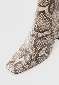 Gros plan sur une botte à bout pointu avec une texture en serpentin beige et noir et un talon carré sur fond blanc.