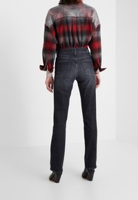 Jeans de tiro alto en gris oscuro con un ajuste slim y diseño de cinco bolsillos, combinados con una camisa a cuadros en rojo y negro con las mangas arremangadas.