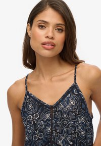 Bezrękawnik w niebiesko-czarny wzór z cienkimi ramiączkami, z motywem paisley i dekoltem w kształcie litery V. Materiał wydaje się lekki i teksturowany.