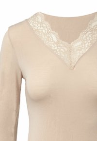 Top nudo a maniche lunghe con scollatura a V in pizzo, caratterizzato da intricati motivi floreali. Tessuto morbido e liscio con una silhouette aderente.