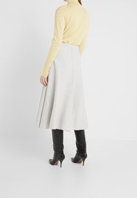 Jasnożółta bluzka z długim rękawem połączona z szarą spódnicą o wysokim stanie w kształcie dzwonu, uzupełniona czarnymi, wysokimi czółenkami.