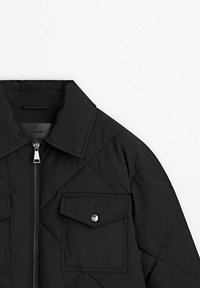 Zwarte gewatteerde jas met een rits aan de voorkant, een gespreid kraag en twee borstzakken met drukknoopsluiting. Gladde textuur met geometrische patronen.