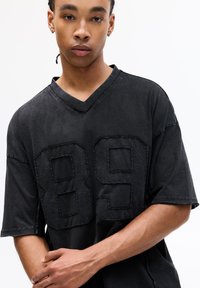Sort oversized t-shirt med v-hals, som har et stort broderet "89" på forsiden. Stofmaterialet har en blød, let struktureret overflade.