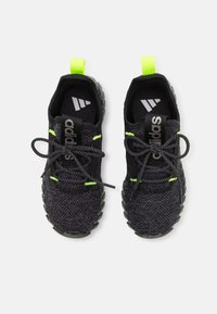 Černé sportovní boty s texturovaným svrškem, neonově zelenými akcenty a černými tkaničkami. Silná podrážka s vzorovaným dezénem pro lepší přilnavost.