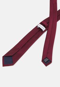Cravate bordeaux en tissu de soie, avec une texture en ribbes diagonales et un revers navy lisse. L'étiquette attachée indique "HER. ONE."