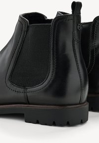 Black leather ankle boots with elastic panels, shown from the side, featuring a textured surface and rugged black rubber soles.