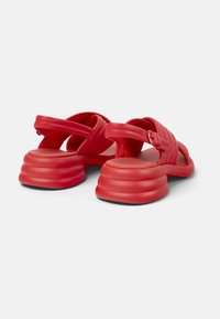 Sandalias de cuero rojo con suela gruesa y estriada. Cuentan con correas cruzadas y un cierre de hebilla en la parte trasera para un ajuste seguro y soporte.