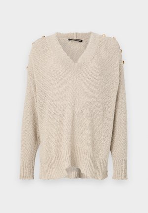 Suéter de punto beige con escote en V, diseño de hombros caídos y dobladillo acanalado. Cuenta con botones dorados en los hombros y una tela suelta y texturizada.