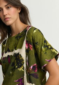 Chemisier floral vert avec des manches courtes, motifs abstraits en rose et jaune, et une coupe décontractée. Tissu léger avec une finition texturée.