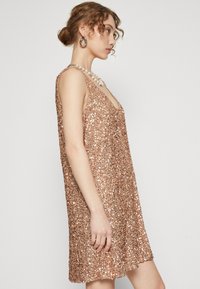 Roze gouden paillettenjurk met een V-hals en een mouwloos ontwerp, met een losse pasvorm en een glanzende textuur die het licht aantrekkelijk weerkaatst.