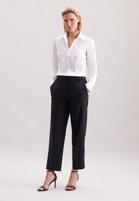 Biała koszula z kołnierzykiem, dopasowany krój, w połączeniu z dopasowanymi czarnymi spodniami i czarnymi sandałkami na obcasie. Gładka faktura i klasyczny styl.