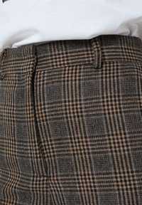 Pantalons à carreaux marron et noir avec une texture lisse, une coupe droite et une taille plate ornée de détails de couture subtils.