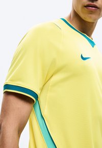 Inimese lähivõte, kes kannab kollast Nike spordisärki, millel on rohelised aktsendid krael, varrukate servades ja küljetuulutusel.