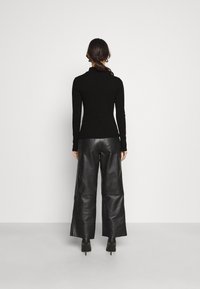 Svart långärmad topp i kombination med högmidjade svarta läderbyxor med vida ben. Outfiten har en figursydd design och en slät textur.