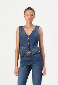 Denim crop vest with V-neckline, five buttons, and front pockets, paired with high-waisted denim jeans. Both in a dark blue wash.