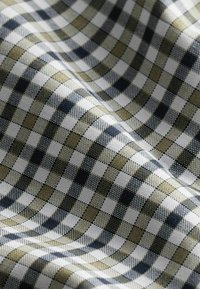 Tessuto con motivo a quadri in verde scuro, blu navy e bianco. La tessitura testurizzata crea una profondità visibile e un contrasto tra i colori.