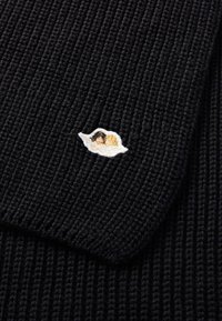 Svart ribbet strikket stoff med et lite brodert design av to figurer i en hvit skyaktig omriss i hjørnet.