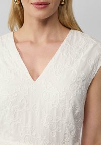 Robe blanche avec un décolleté en V, des manches courtes et une broderie florale complexe. Texture lisse avec des détails en fil délicats.