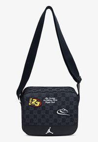 Juodas kryžminis krepšys su reguliuojama juostele, turintis margintą dizainą, siuvinėtus logotipus ir spalvingus pleistrus. Lygus paviršius ir užtrauktuko uždarymas.