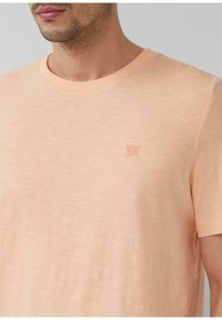 Perzikkleurig T-shirt met korte mouwen van zachte stof, met een ronde halslijn en een klein, tone-on-tone logo op de borst.