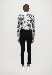 Camiseta de manga larga con patrón de cebra, vaqueros ajustados negros, zapatillas blancas. Incluye detalles en colores contrastantes y un logo en la parte superior.