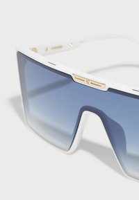 Vita oversized solglasögon med blå gradientlinser och guldaccenter på ramen. Har en geometrisk design och jämn yta.