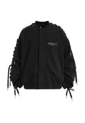 Chaqueta bomber negra con detalles de cordones en las mangas, bolsillos con cremallera, dobladillo y puños acanalados, y un pequeño parche rectangular en el pecho delantero.