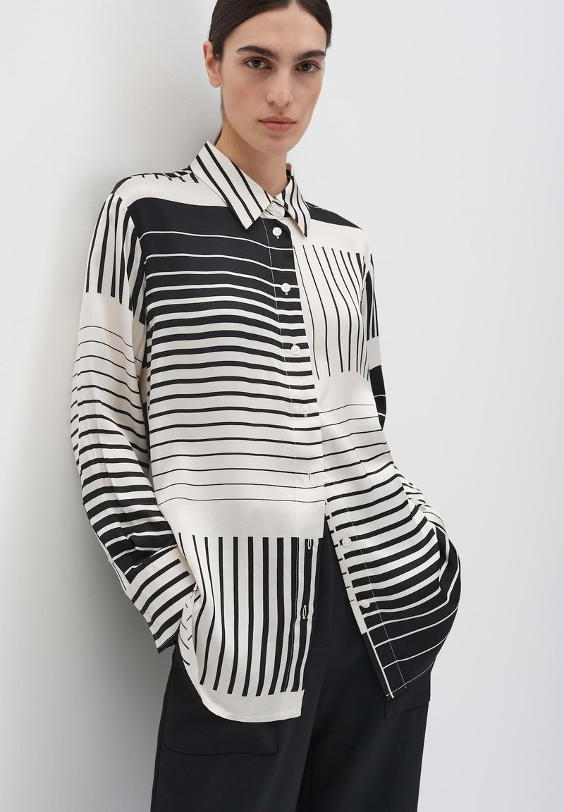 Schwarz-weiß gestreifte Bluse mit Knopfverschluss vorne, langen Ärmeln und seidiger Textur. Mit unterschiedlich breiten Streifen und klassischem Kragen.