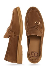 Mocasines de ante marrón con costura, diseño de mocasín y un pequeño detalle decorativo en la parte delantera. Incluye suela de goma.