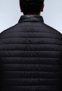 Rövid göndör hajú férfi fekete steppelt dzsekit visel, hátulnézetből, a gallér részleteivel és a vízszintes varrással.