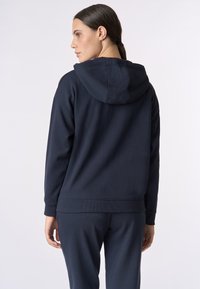 Felpa con cappuccio blu navy, con polsini e orlo a coste, caratterizzata da una texture morbida e un design minimal, mostrata da dietro.