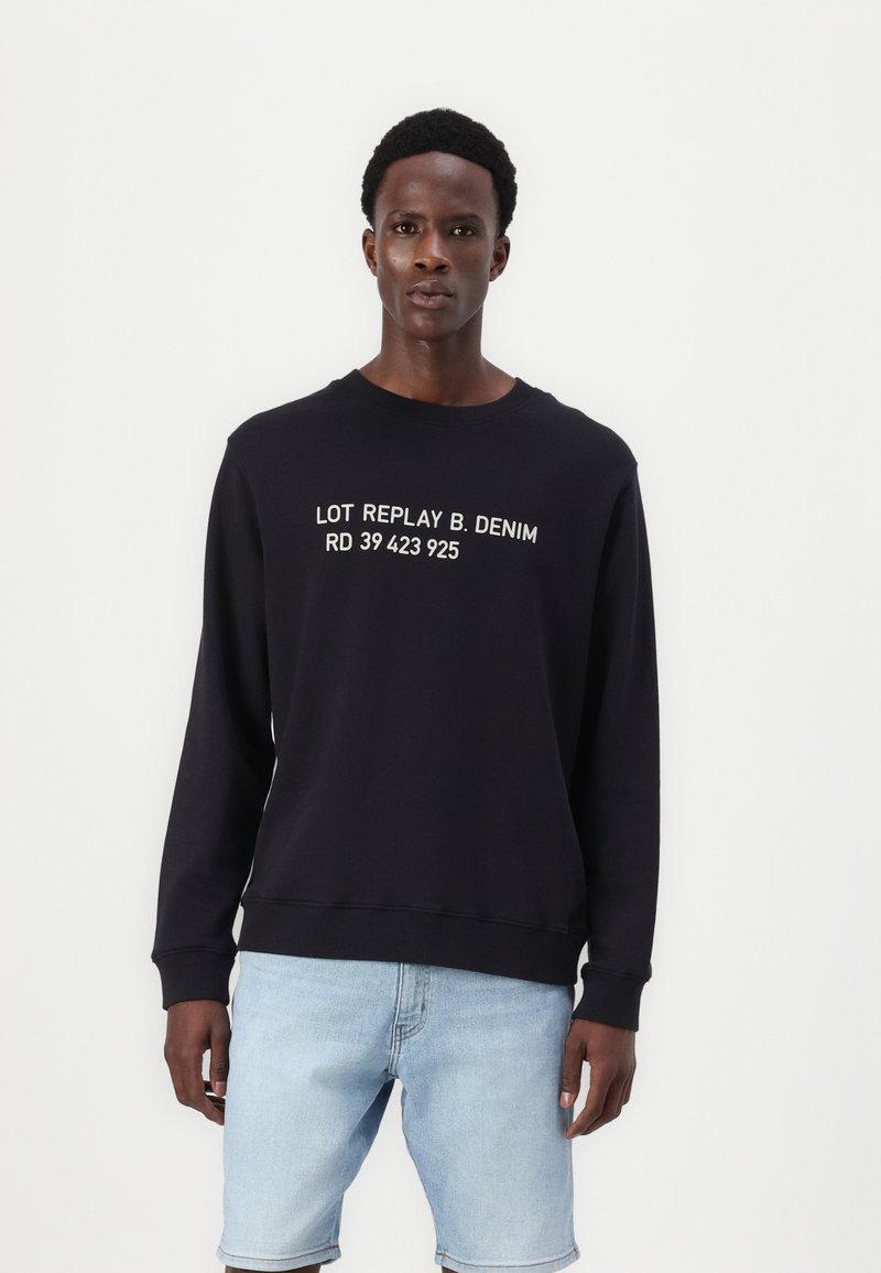 Fekete pulóver, fehér "LOT REPLAY B. DENIM RD 39 423 925" felirattal, kerek nyakkivágással és bordázott mandzsettákkal, világoskék sorttal párosítva.