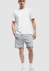 Hvid bomulds t-shirt med korte ærmer parret med lysegrå sweatshorts, der har en elastisk talje og sidelommer.