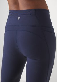 Námořnické modré legíny vyrobené z elastického materiálu, s vysokým pasem, plochými švy a malou kapsou na zip vzadu.