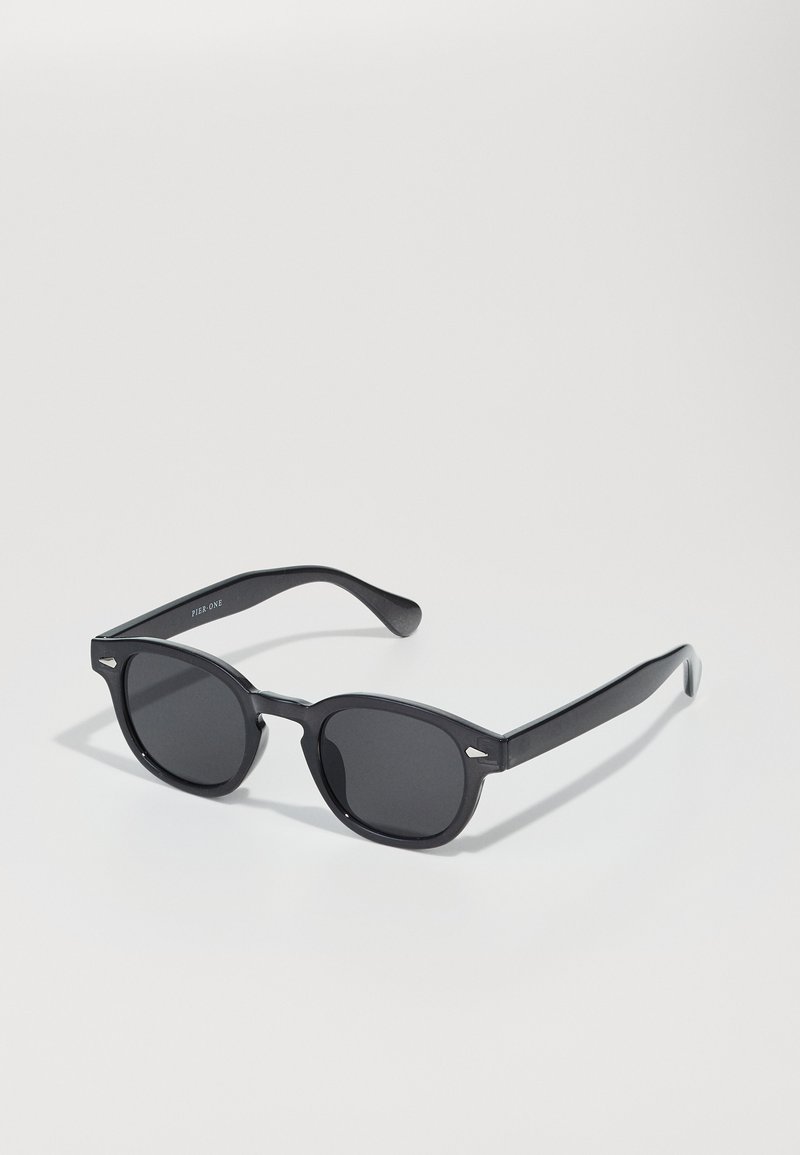 Black sunglasses with rounded frames, dark lenses, and subtle metallic accents on the frame. Smooth plastic material, minimalistic design.