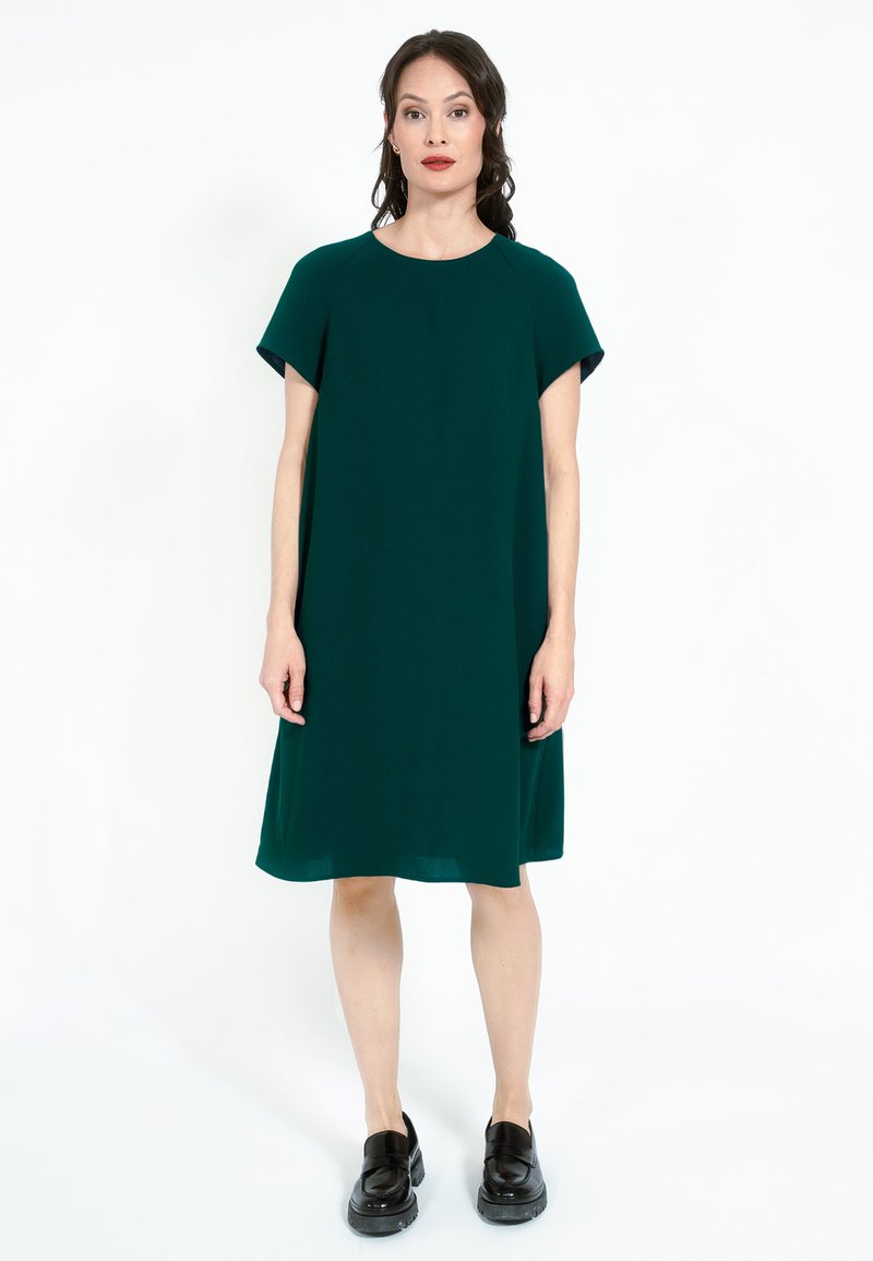 Rochie verde, până la genunchi, dintr-o țesătură netedă, cu mâneci scurte și guler rotund. Purtați cu mocasini negri. Design simplu, fără modele.