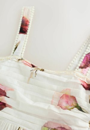 Floral-patterned dress with pale fabric, featuring pink and maroon roses, textured pleats, and decorative pom-pom trim on straps.