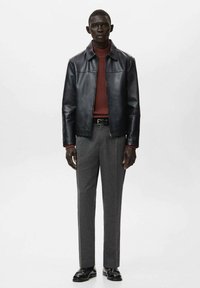 Czarna skórzana kurtka z wysokim kołnierzem, bordowy sweter prążkowany i szare spodnie w wzory. Model nosi czarne buty, stoi na białym tle.