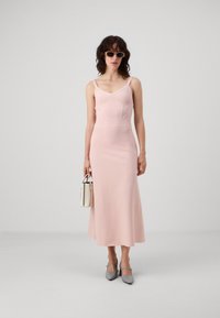 Abito midi fitted color rosa pallido con scollatura a V, spalline larghe e dettagli in rilievo sul busto. Abbinato a una borsa bianca e ballerine grigie a punta.